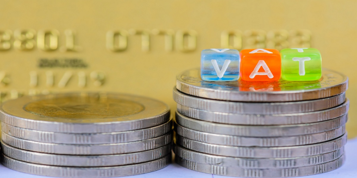 Photo of VAT (Value Added Tax) letter cubes on stacks of coins with gold credit card background