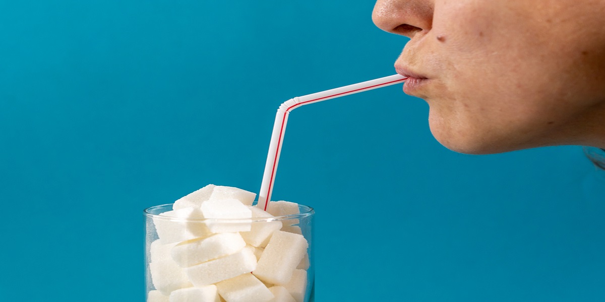 Profile of a woman drinking through a red striped straw, the glass is full of sugar cubes. Highlighting the need for a sugar tax on certain drinks.