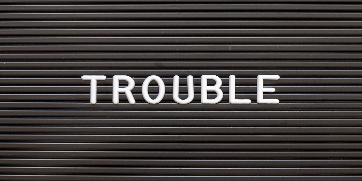Black felt board background, word 'trouble' in white capital letters at the forefront.