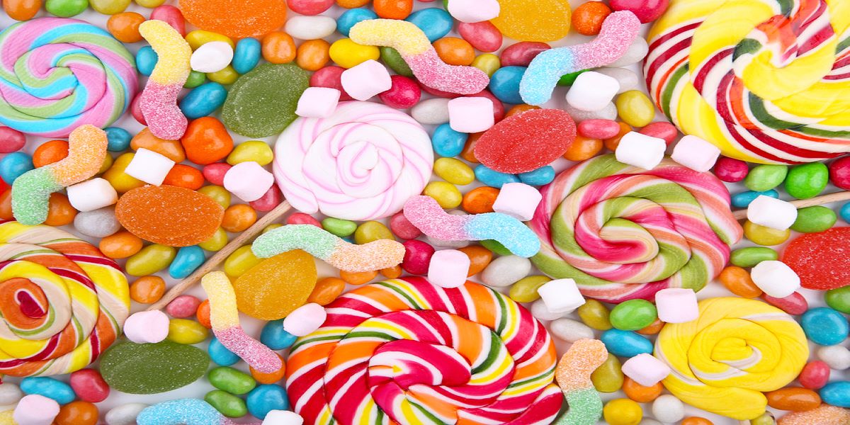 Pile of assorted colourful sweets, including mini marshmallows, fizzy snakes, jellies and round spiraled lollipops.