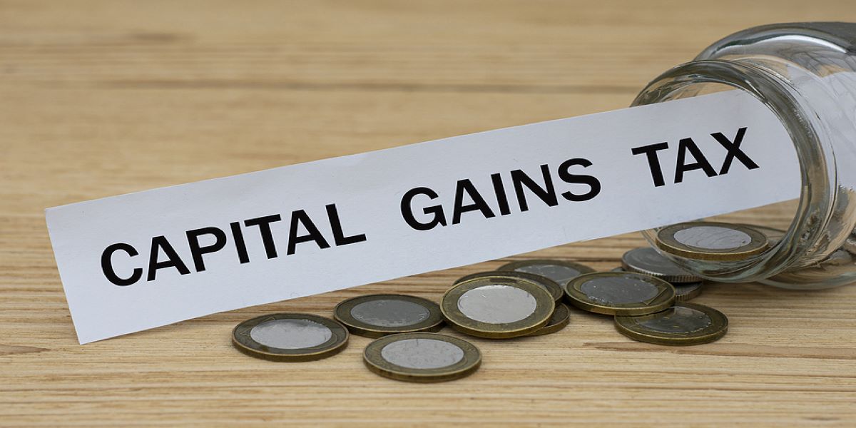Photo of a glass jar lying on its side 2 pound coins spilling out and a white paper label sticking out of the top saying capital gains tax.