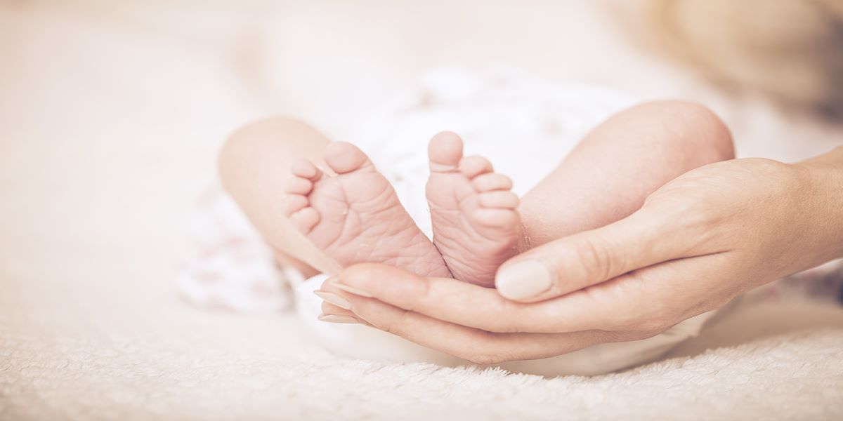 Soles of a newborn baby's feet being held by a woman's right hand.
