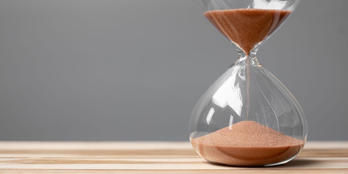 Glass sand timer on a wooden table with a grey background, positioned to the right of the shot.