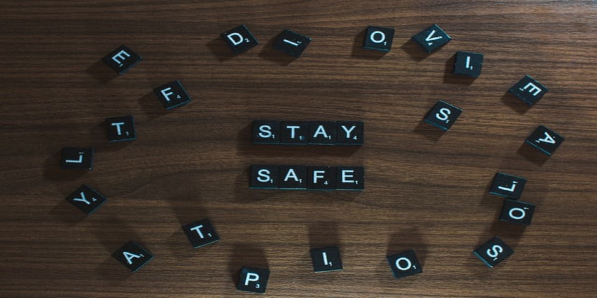 Black letter tiles with white letters spelling stay safe, surrounded by random arrangement of other letters on a wooden surface.